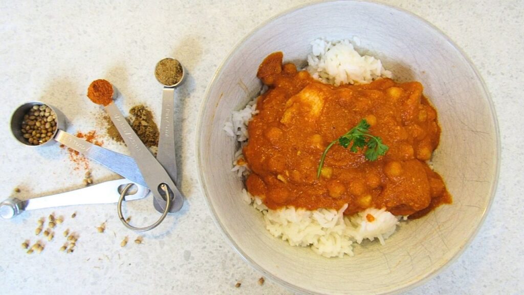 miska z ryżem i indyjska potrawka z kurczaka oraz łyżeczki z przyprawami garam masala, chilli i kolendra
