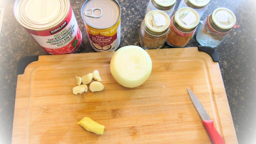 deska do krojenia z cebulą, czosnkiem i imbirem oraz puszki z pomidorami na indyjską potrawkę z kurczaka