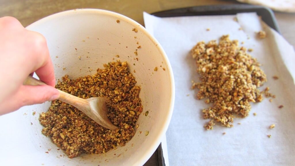 ręką przekładająca granolę z miski na blaszkę do pieczenia
