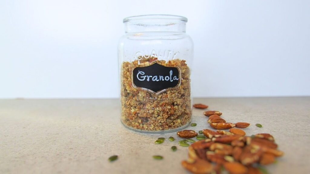 zdrowa granola w słoiku z rozsypanymi orzechami i pestkami dyni