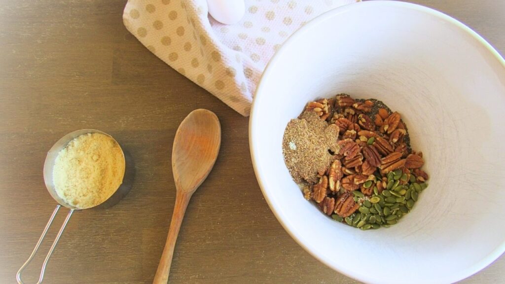 miska ze składnikami na granolę a obok drewniana łyżka i naczynie z mąką migdałową