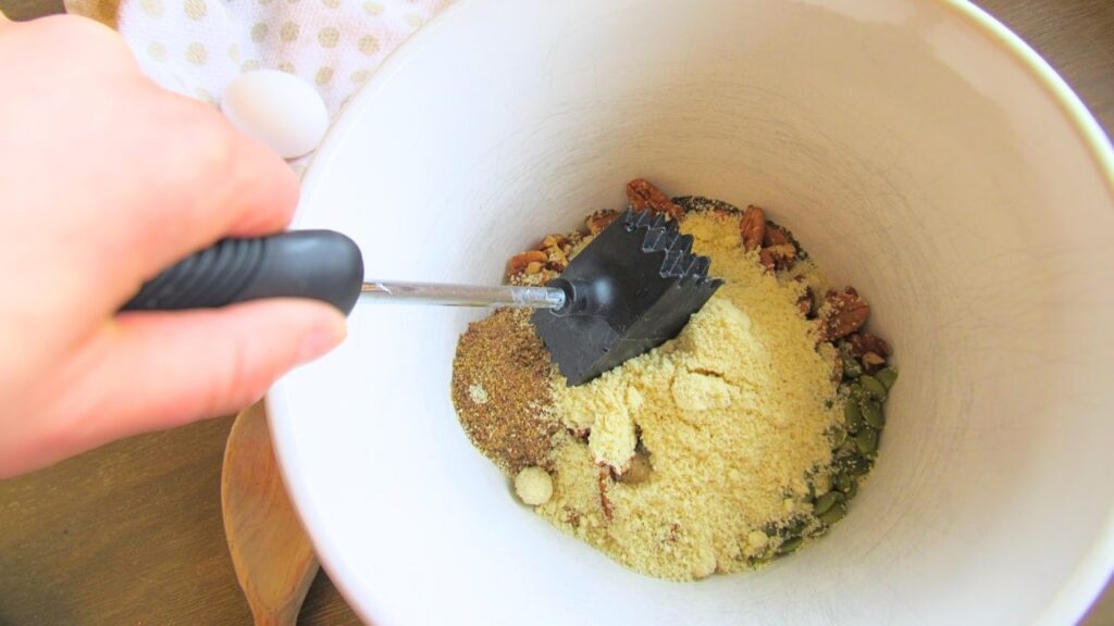 ręka z tłuczkiem rozdrabniającym składniki na granolę w misce