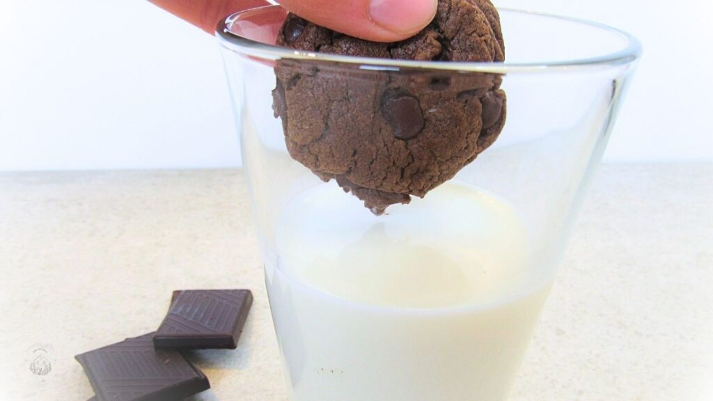 szklanka mleka i ręka trzymająca czekoladowe ciasteczko