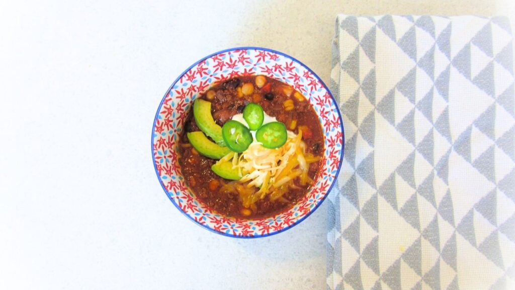miska z chili con carne przyozdobionym serem, awokado i papryczkami jalapeno