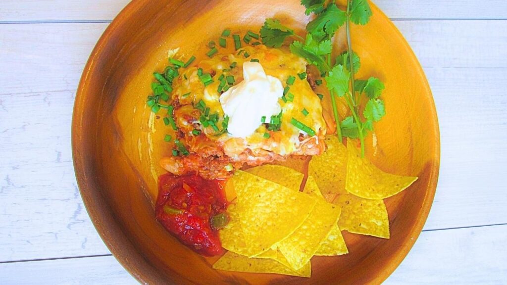 zapiekanka z mięsem mielonym po meksykańsku w misce drewnianej z chipsami tortilla, śmietaną i świeżą kolendrą