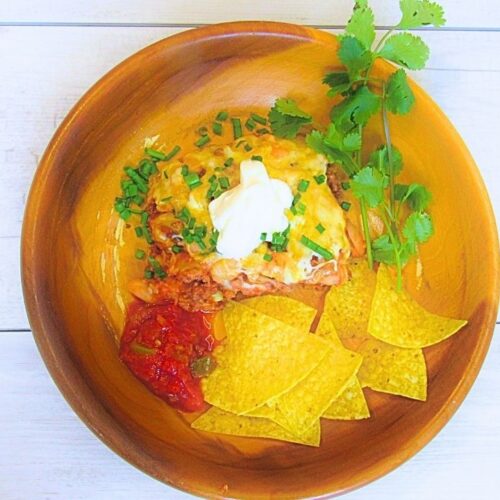 zapiekanka z mięsem mielonym po meksykańsku w misce drewnianej z chipsami tortilla, śmietaną i świeżą kolendrą