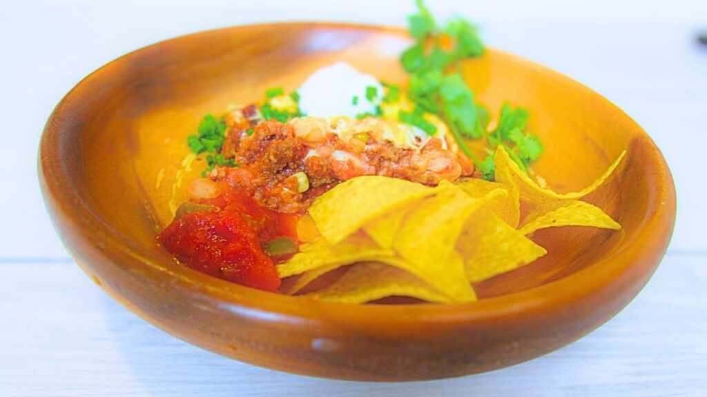 zapiekanka z mięsem mielonym po meksykańsku w misce drewnianej z chipsami tortilla, śmietaną i świeżą kolendrą