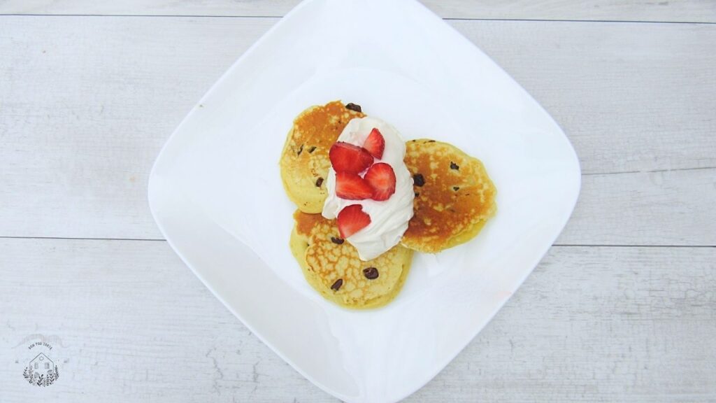 Puszyste amerykańskie pancakes z czekoladą, a na stronie truskawki i bita śmietana