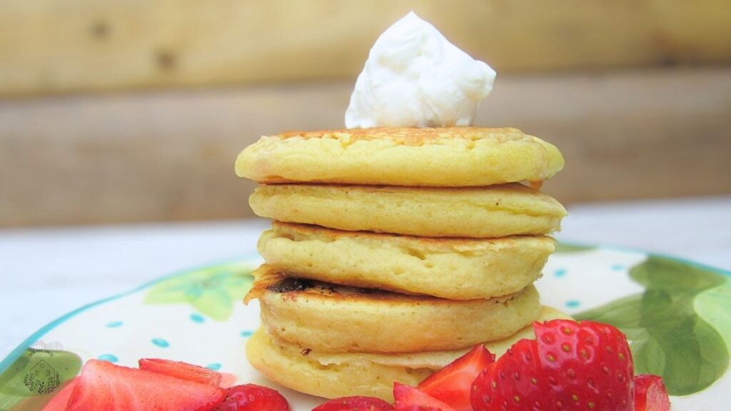 Puszyste amerykańskie pancakes z czekoladą, a na stronie truskawki i bita śmietana