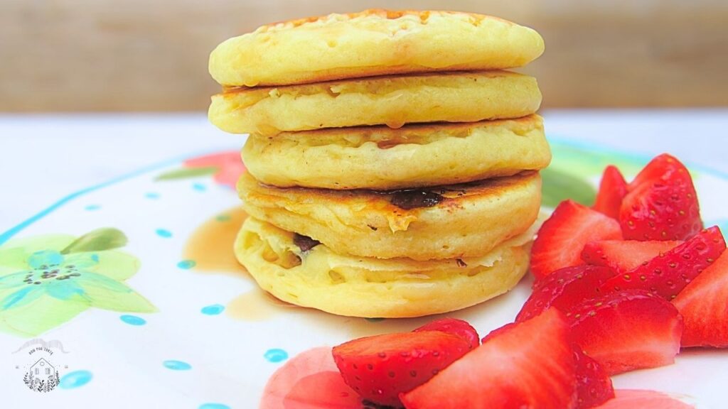 Puszyste amerykańskie pancakes z czekoladą, a na stronie truskawki i syrop klonowy