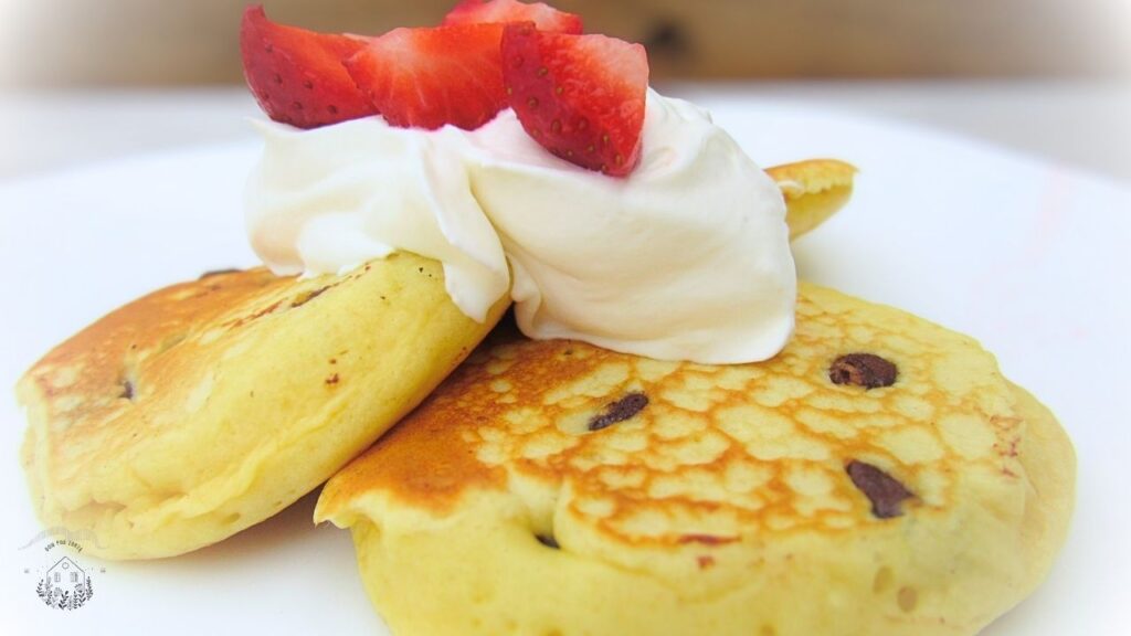 Puszyste amerykańskie pancakes z czekoladą, a na stronie truskawki i bita śmietana