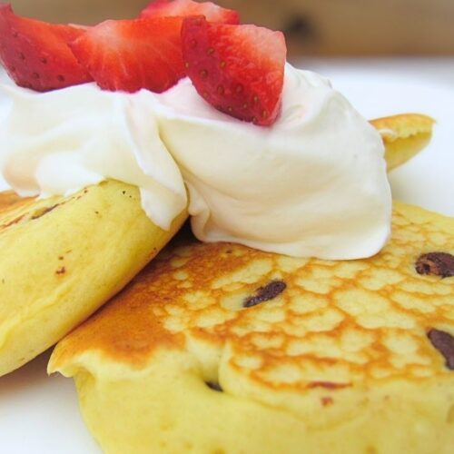 Puszyste amerykańskie pancakes z czekoladą, a na stronie truskawki i bita śmietana