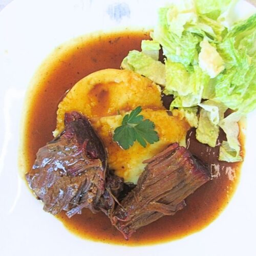 pieczeń wołowa na białym talerzu w sosie z ziemniaczkami