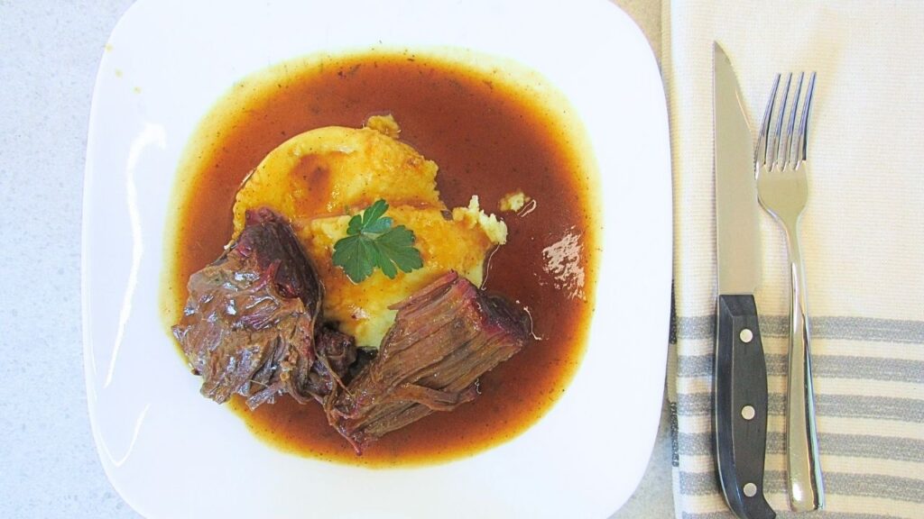 pieczeń wołowa na białym talerzu w sosie z ziemniaczkami