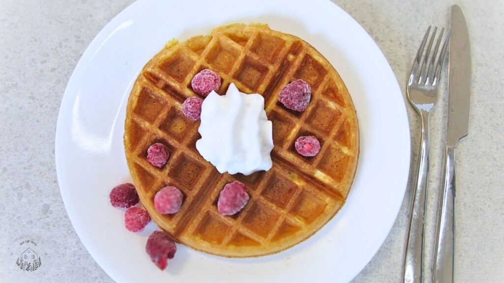 Gofry na zakwasie z bitą śmietaną i malinami na białym talerzu