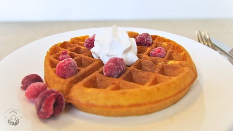 Gofry na zakwasie z bitą śmietaną i malinami na białym talerzu