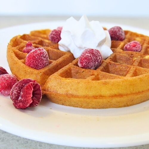 Gofry na zakwasie z bitą śmietaną i malinami na białym talerzu