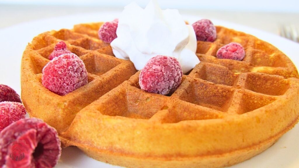 Gofry na zakwasie z bitą śmietaną i malinami na białym talerzu